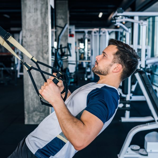 Side view of athlete doing exercises for back and arms with suspension straps.